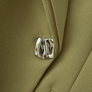 Détail d'une broche en métal argenté irrégulier sur un tissu de costume vert olive