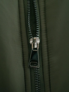 Close-up of durable silver metal zipper on an olive green quilted cotton jacket