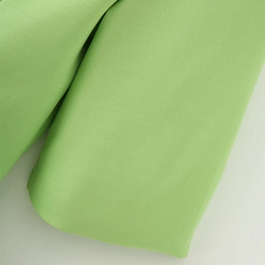 Close-up detail of light green textured woven fabric and stitching on blazer