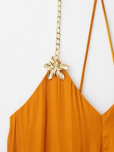 Détail d'une robe midi en satin gingembre avec chaîne dorée et fleur métallique