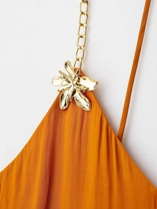 Détail de robe en satin orange avec boucle fleurie dorée et bandoulière en chaîne