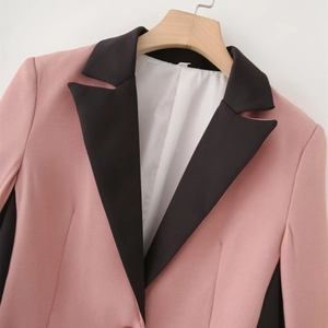 Detail of pink blazer with black notched lapels and side panels on wooden hanger