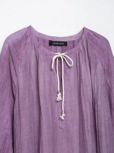 Détail du chemisier en lin violet avec cordon blanc, perles en bois et pompons