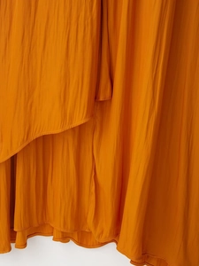 Détail du tissu satiné plissé orange avec couture d'ourlet délicate et texture fine