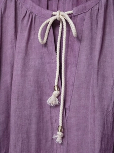 Détail de robe en lin tie-dye violette montrant le col en V avec cordon et gland décoratif