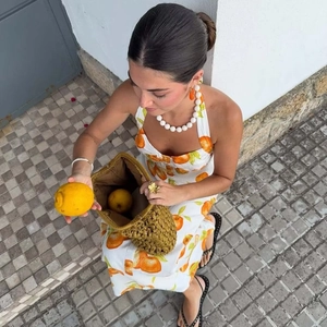 Linen halter neck dress with orange prints and straw bag for a summer vacation look
