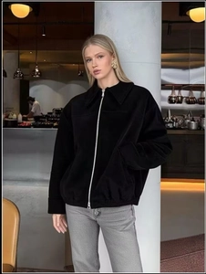 Detail of a black suede bomber jacket featuring a classic collar and metallic front zipper
