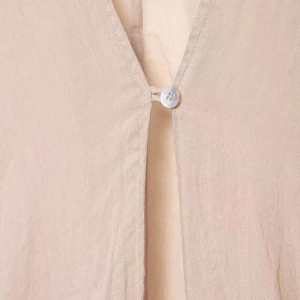Gros plan d'un haut en lin ramie beige avec col en V et fermeture à bouton perlé