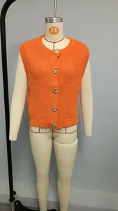 Detail of bright orange knit vest featuring golden textured buttons and ribbed fabric
