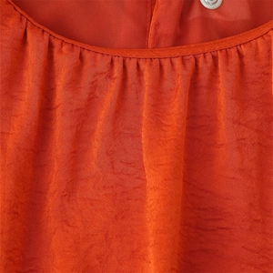 Détail de l'encolure plissée sur une robe orange sans manches en tissu texturé