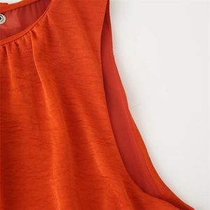 Détail de la robe sans manches rouge-orange montrant le col plissé et le bouton métal