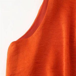 Gros plan d'une robe orange sans manches avec texture plissée et liseré en satin élégant
