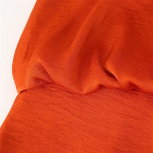 Détail de la robe plissée orange montrant la texture du tissu crêpé et les fronces