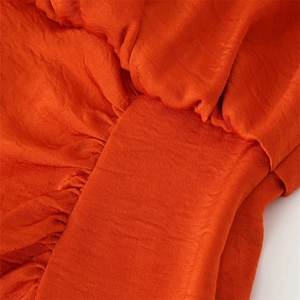 Gros plan sur le tissu satiné orange montrant les plis détaillés et la texture soyeuse
