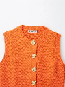 Close-up of orange knit vest featuring unique gold shell-shaped buttons and neckline detail