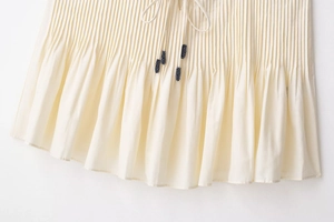 Close-up of pleated beige skirt featuring drawstring with tassels and ruffled hem detail