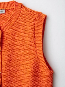 Macro shot of orange sleeveless knit vest with textured grain fabric and ribbed edges