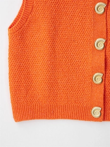 Detail of orange textured knit vest featuring golden spiral seashell-shaped metal buttons