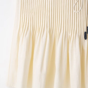 Beige pleated skirt featuring fine accordion folds and blue beaded tassel detail