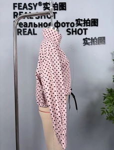 Detail view of pink jacket with black polka dots featuring stand collar and drawstring hem