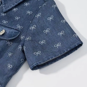 Detailed view of dark blue denim shirt featuring bow patterns and rhinestone floral button