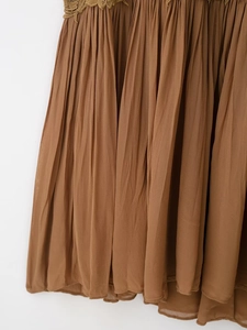 Detailed close-up of brown pleated fabric with delicate lace crochet embroidery trim