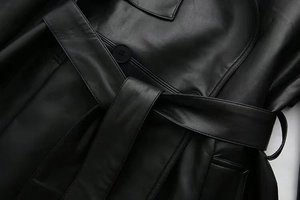 Detail of black faux leather trench coat showing waist belt and premium stitching texture