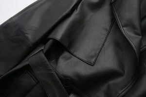 Close-up of black faux leather trench coat showing collar, shoulder seam and belt details