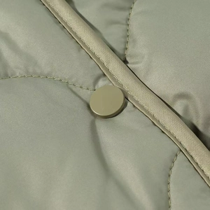 Detail of light olive quilted jacket featuring curve stitching and matte snap button