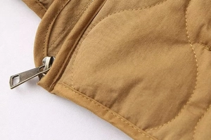 Detail of brown quilted jacket showing premium metal zipper and curved stitching texture