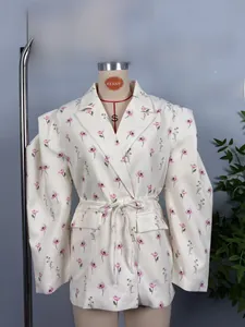Détail d'un blazer blanc à fleurs roses avec ceinture à la taille et épaulettes