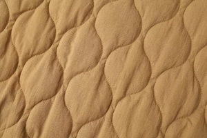 Detailed macro view of onion-shaped wavy quilting on camel washed cotton jacket fabric