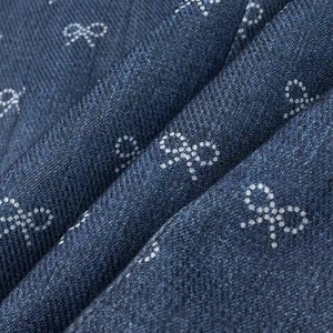 Macro shot of dark blue denim fabric with white bow patterns and twill texture detail