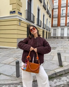 Detail of a brown quilted jacket with drawstring design and chic caramel leather handbag