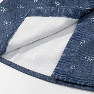 Detailed close-up of dark blue bow-print denim dress hem showing stitching and soft lining