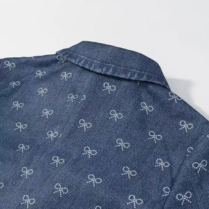 Detailed close-up of blue denim dress featuring white polka dot bow patterns on collar