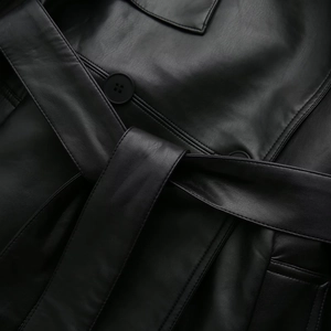 Detail of black faux leather trench coat with grain texture, matching buttons and belt