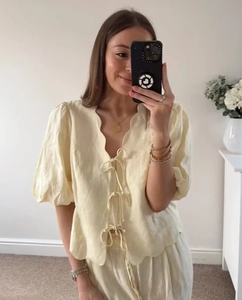 Detail of light yellow linen set featuring scallop trim and tie-front puff sleeves