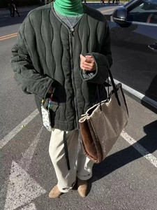 Deep olive green quilted jacket worn with a fuzzy cream tote bag in an outdoor street setting