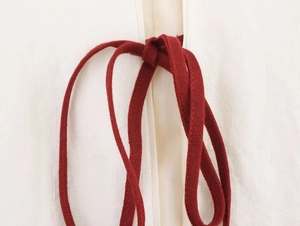 Close-up detail of white linen fabric with deep red woven drawstring tie closure