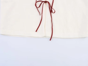 Detail of red string bow tie on creamy white embroidered linen shirt jacket