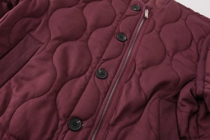 Close-up of maroon wavy quilted jacket featuring black buttons and silver metal zipper