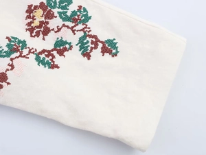 Close-up of intricate red floral cross-stitch embroidery on white linen fabric