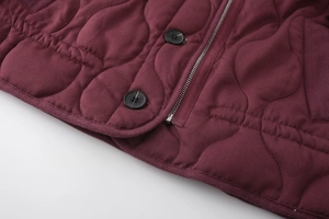 Detail of burgundy quilted jacket showing resin buttons, zipper, and wavy stitching