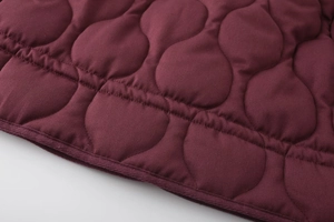 Detailed macro view of burgundy quilted fabric with wave stitching and braided edge trim