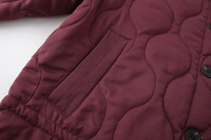 Close-up of quilted burgundy jacket with herringbone trim and black button details