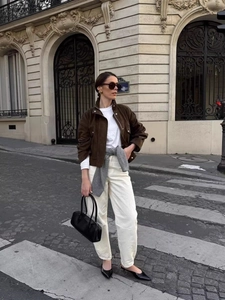 Chic women's brown suede jacket with white trousers and black tote bag in city street view
