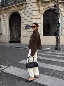 Women's dark brown suede jacket styled with white straight pants and black handbag