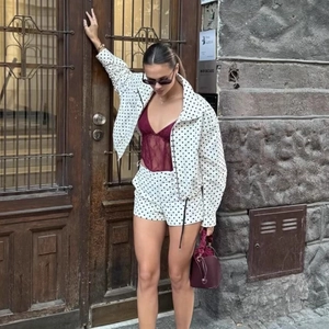 Women's chic white polka dot puff sleeve jacket with matching shorts set on a street model