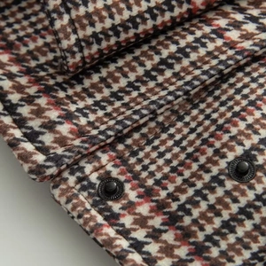 Detailed shot of houndstooth wool fabric with black metal snap buttons and red accents